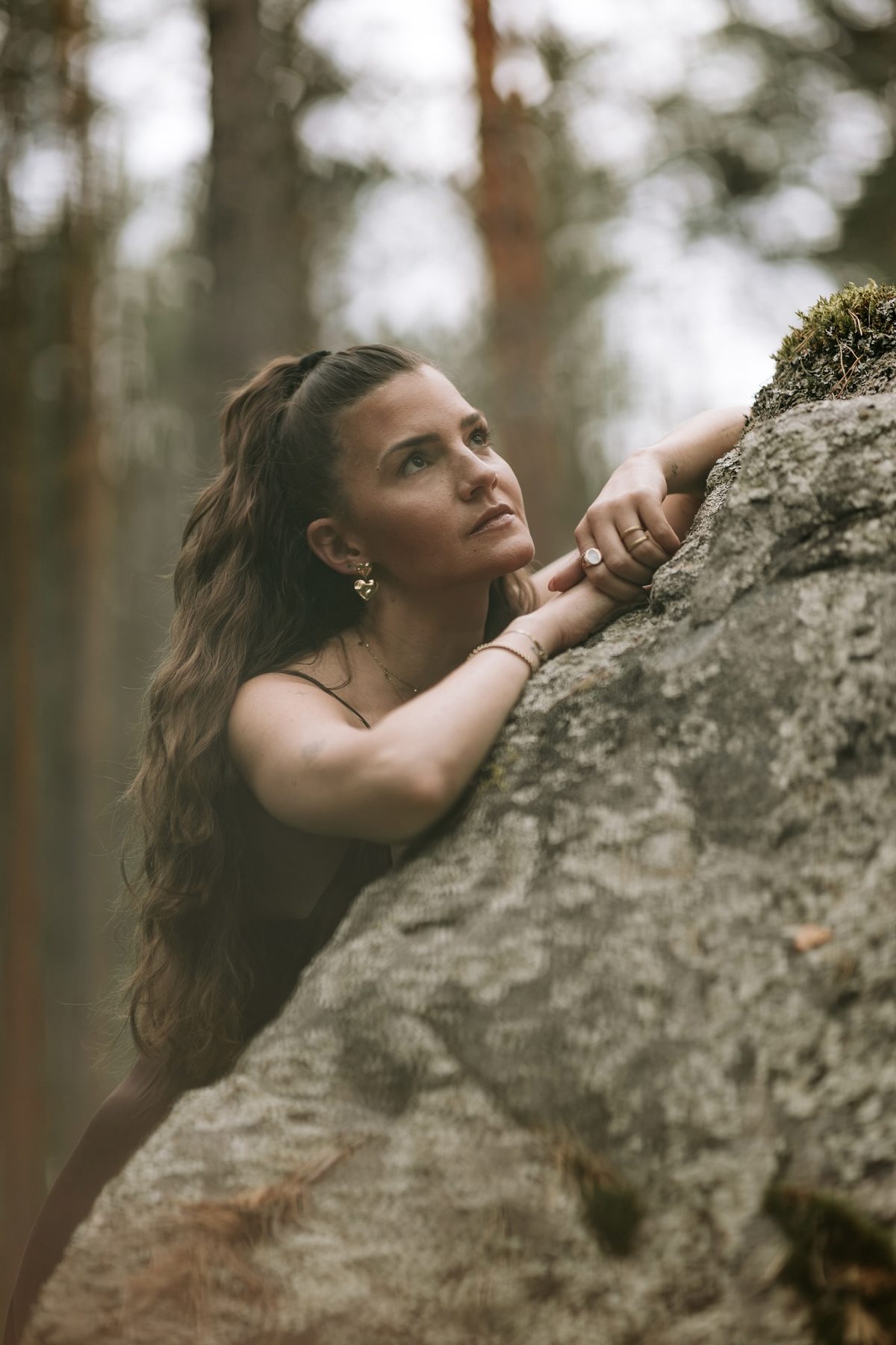 Selina lehnt an einem Felsen und schaut in die Baumkronen