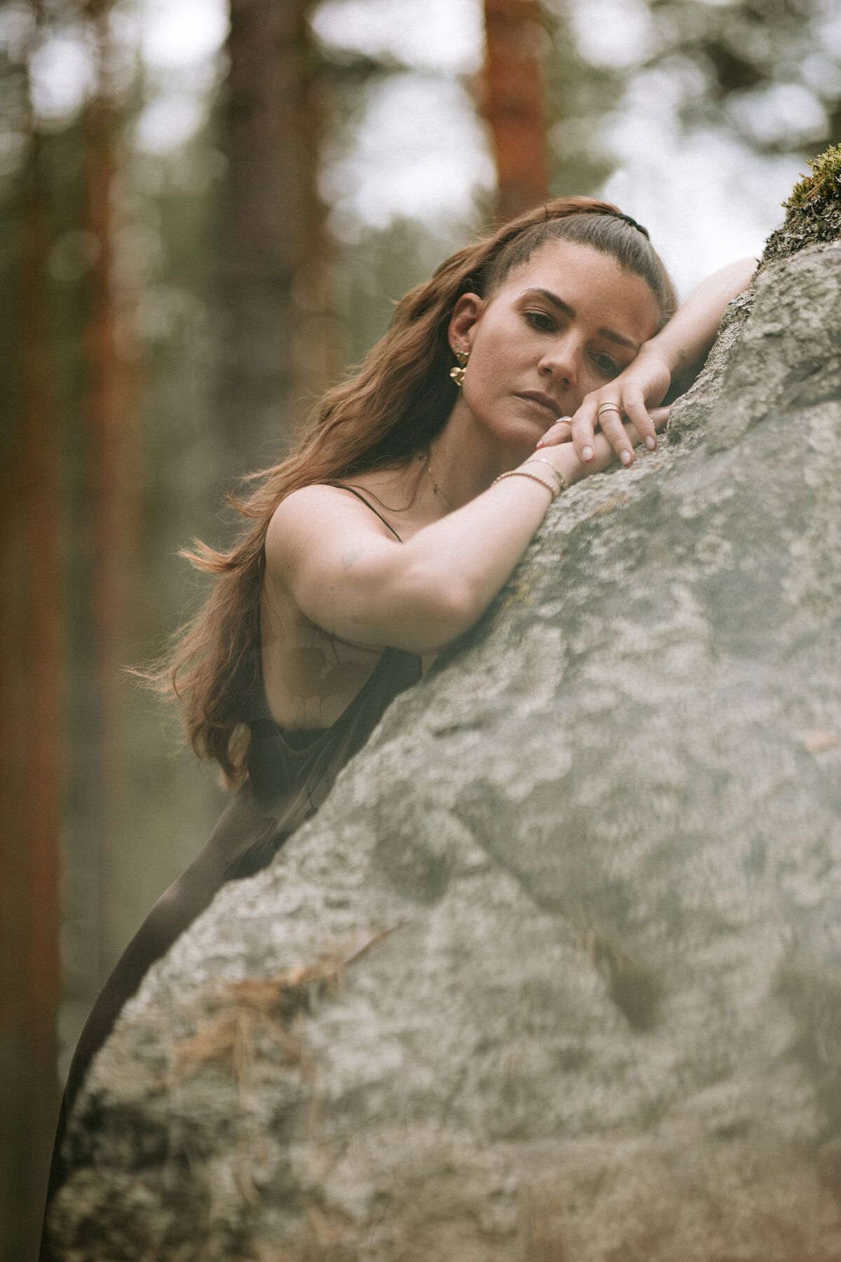 Selina lehnt nachdenklich an einem Felsen im Wald