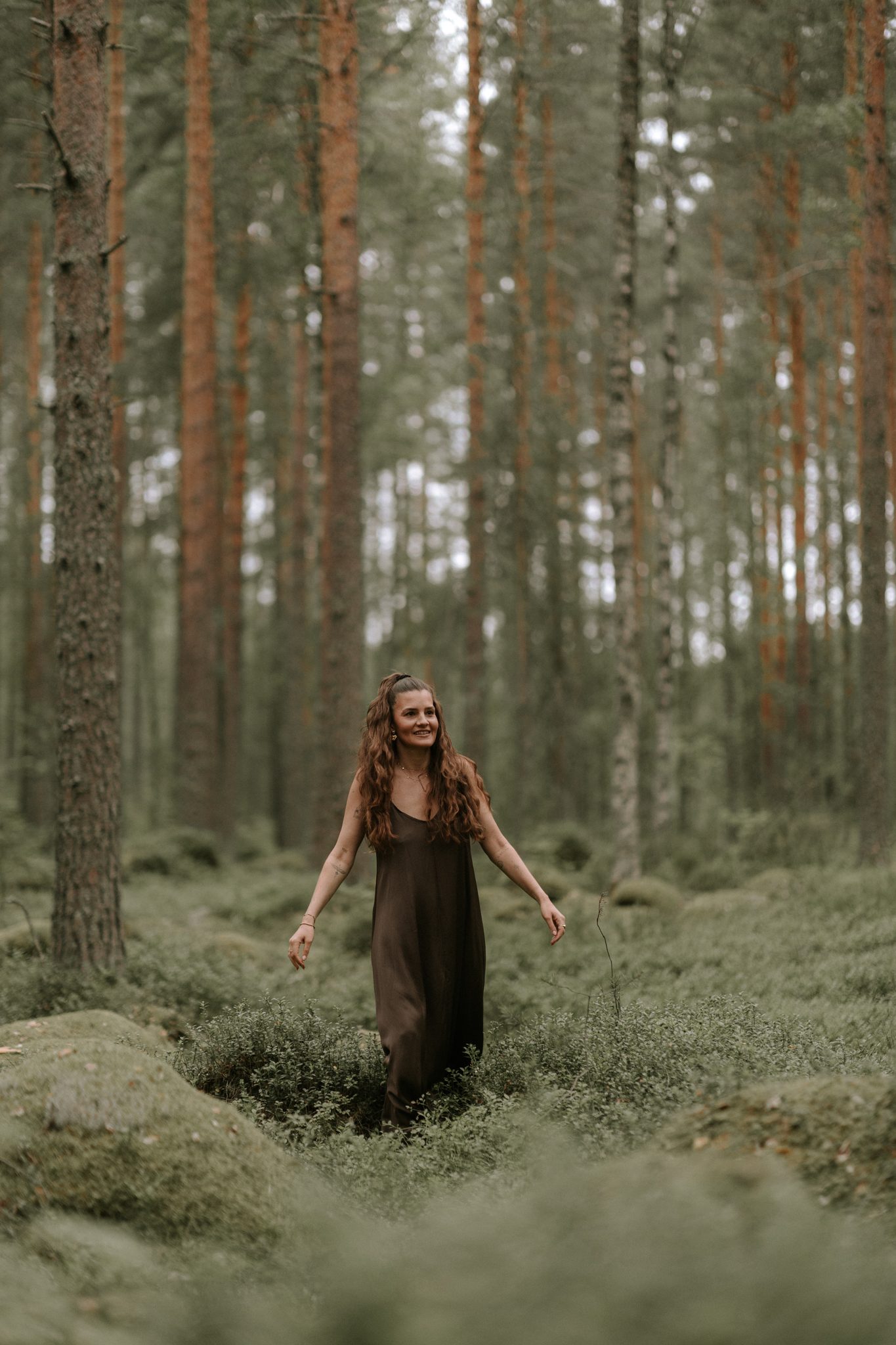 Selina geht lächelnd durch einen Kiefernwald