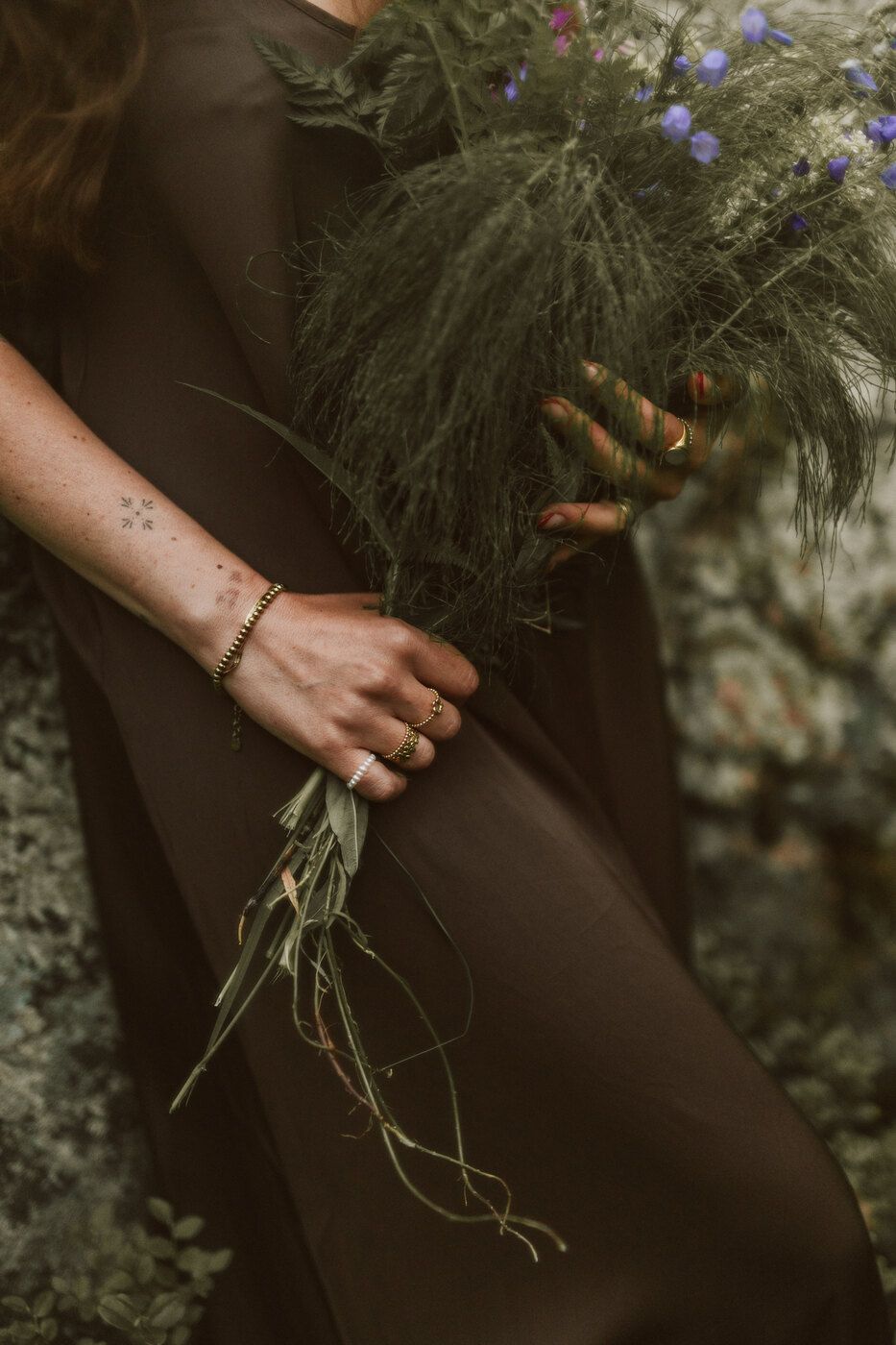 Hände halten einen Strauß Wildblumen und Gräser vor einem braunen Kleid